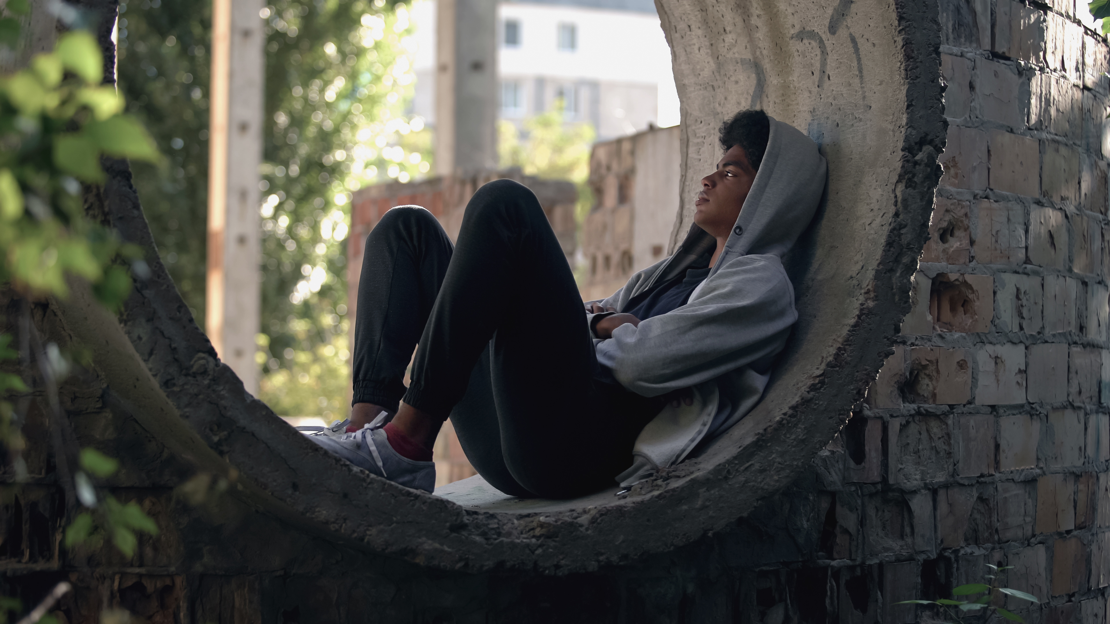Trauriger einsamer Student im Kapuzenpulli, der allein in einem verlassenen Gebäude sitzt.