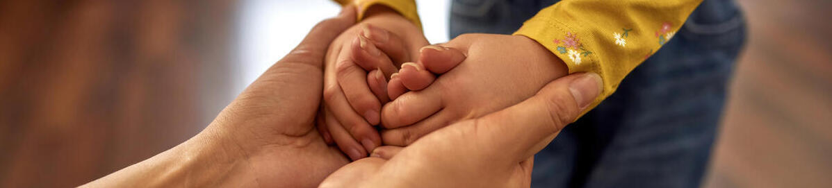 Frauenhände halten liebevoll kleine Kinderhände und schaffen Vertrauen