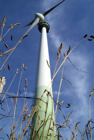Windenergieanlage vor blauem Himmel, betrachtet von unten aus dem hohen Gras.