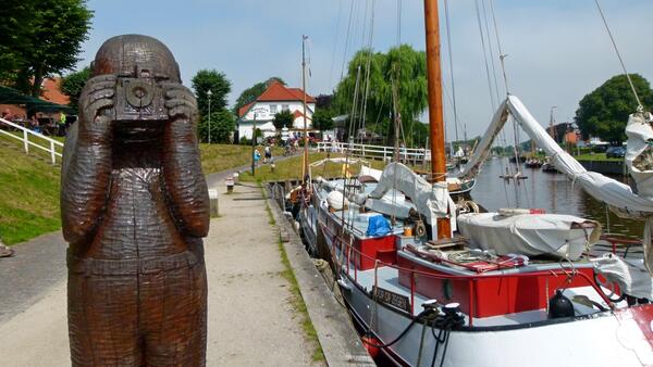 Eine Statue am Museumshafen in Caroli8nensiel h&auml;lt eine Kamera vor das Gesicht.