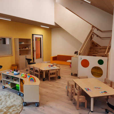 Gruppenraum mit Spieleecke, Gruppentischen und einer Treppe im HIntergrund