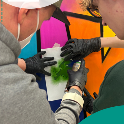 Zwei Jungs mit Maske spr&uuml;hen eine Wand mit Schablone an