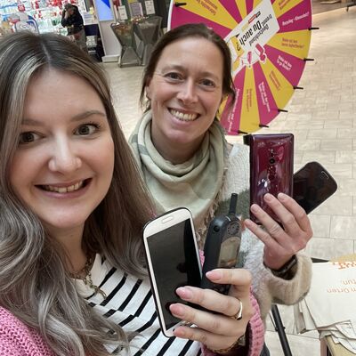 Vanessa D&uuml;ring und Antje Jansen vom Abfallwirtschaftsbetrieb sind mit Handys in der Hand zu sehen, im Hintergrund steht ein Gl&uuml;cksrad.