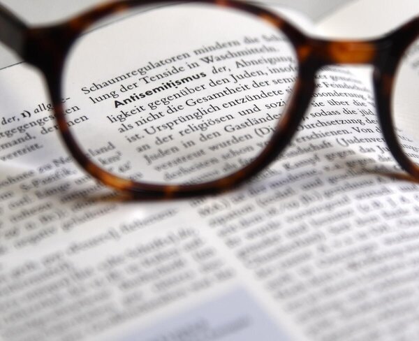 Eine Brille liegt auf einem aufgeschlagenen Buch. Durch das Brillenglas ist das Wort &raquo;Antisemitismus&laquo; scharf zu erkennen, w&auml;hrend der restliche Text unscharf bleibt.